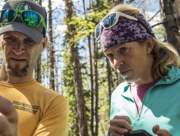 Two adventure scientists check and log data from a checkpoint in the woods