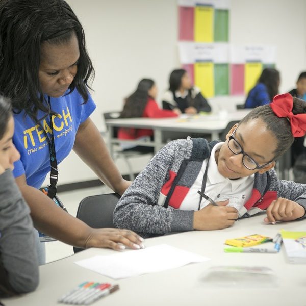 A female teacher assists two female students with their assignments in a classroom