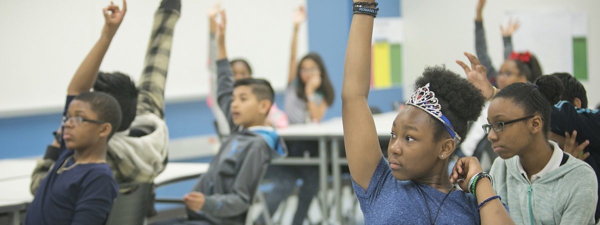 Students in a classroom raise their hands to answer a question