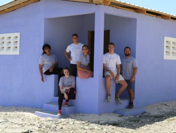 New Story team sitting on the steps of a home purple painted house that they built in Haiti