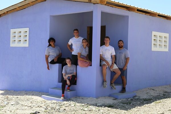 New Story team sitting on the steps of a home purple painted house that they built in Haiti