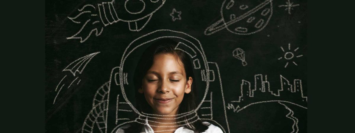 Little girl in front of a blackboard with an astronaut helmet drawn around her in chalk