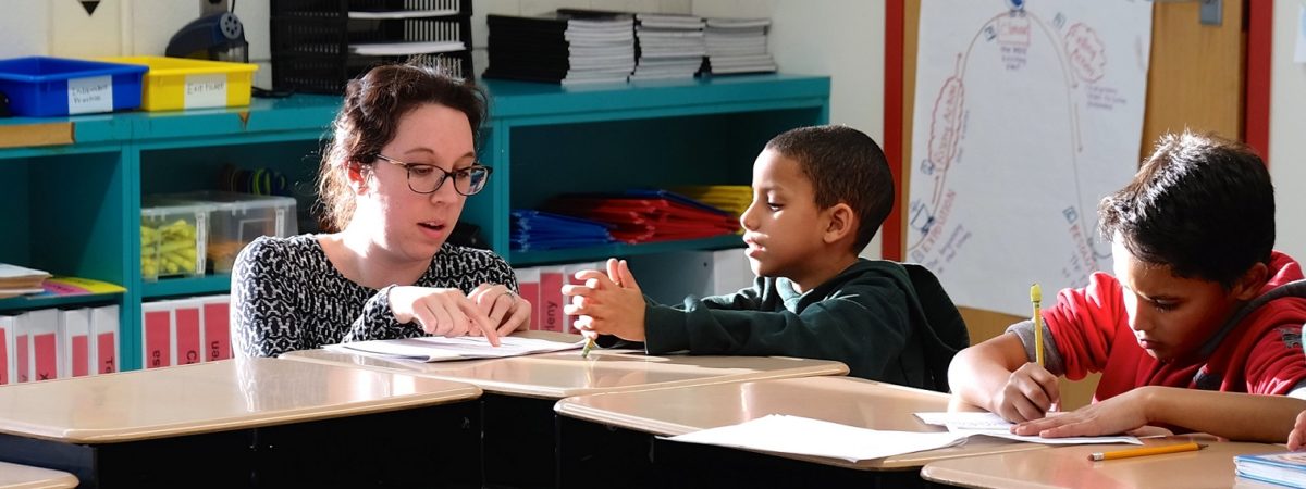 Teacher assists two young students at their desk