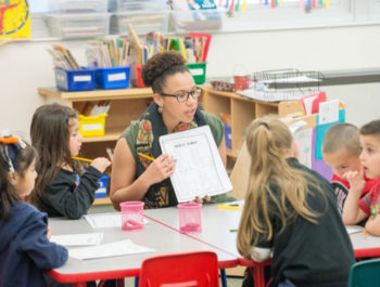 Female teacher in a classroom sits at a table with students