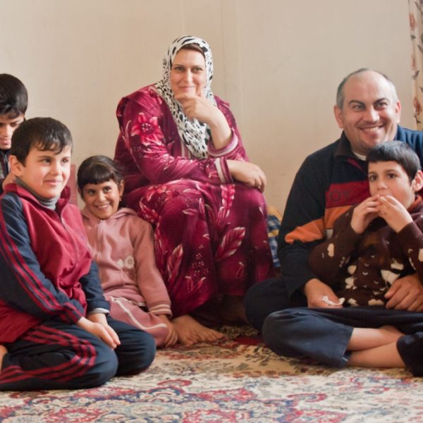 Immigrant family sits on the floor in their living room smiling