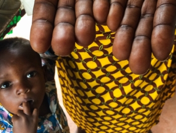 Woman hold outs her hands to show her finger prints, a little boy stands close by