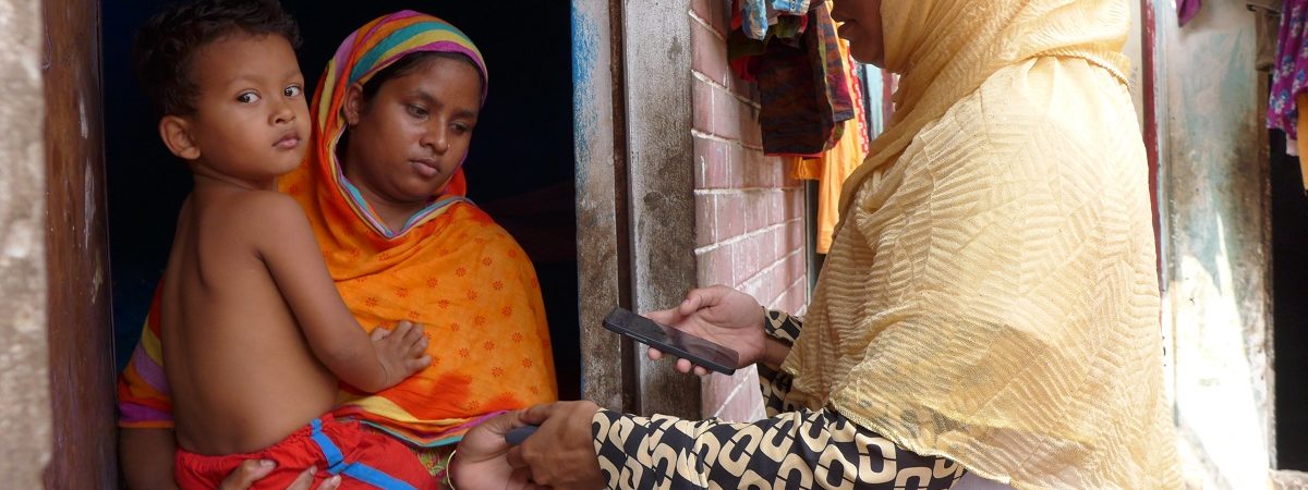 Indian woman holding a baby in a doorway has finger printed by another Indian woman