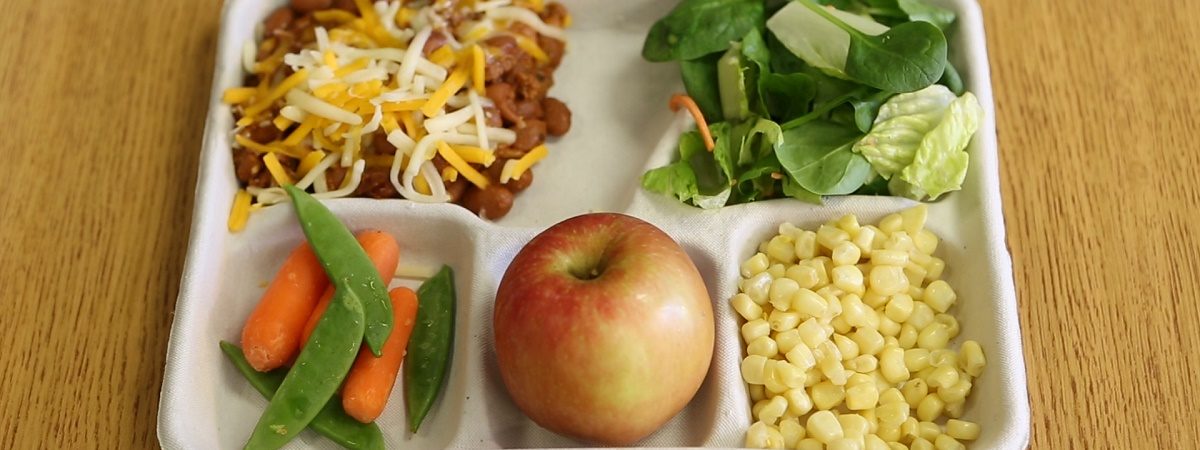 Picture of a school lunch tray featuring an apple. corn, salad, chili and green beans