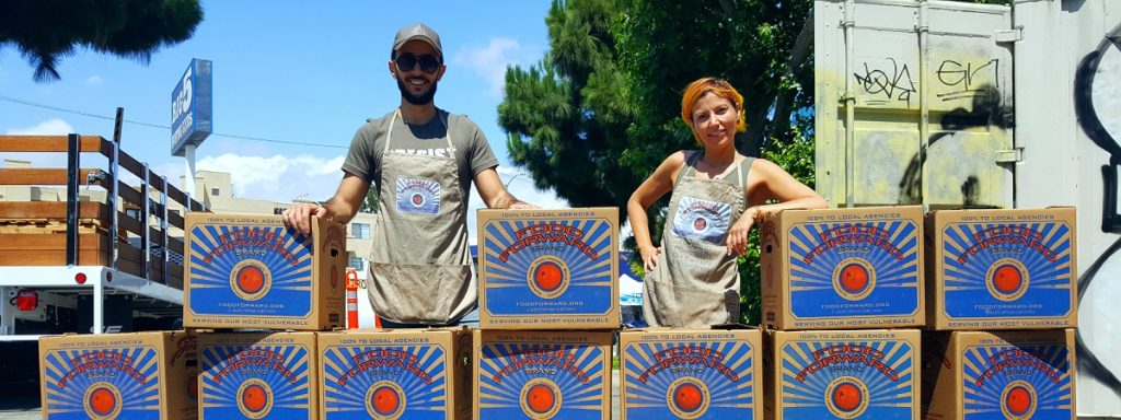 Two food forward farmers stand among towering boxes filled with produce