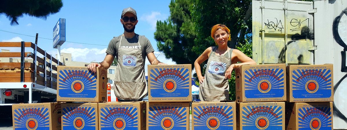 Two food forward farmers stand among towering boxes filled with produce