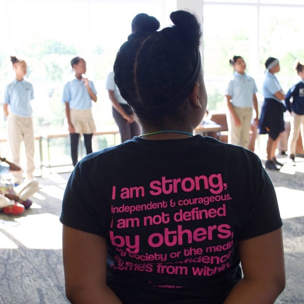 Young black girl stands with her back to the camera wearing an inspiring t-shirt with a message that 