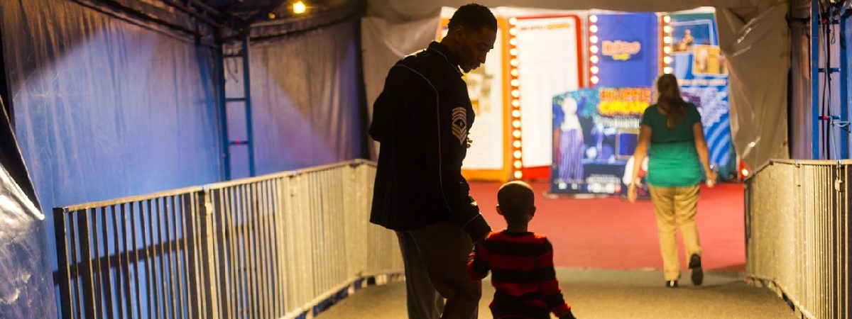 Father and son walk down the halfway smiling at one another. Bright lights fill the circus like room.