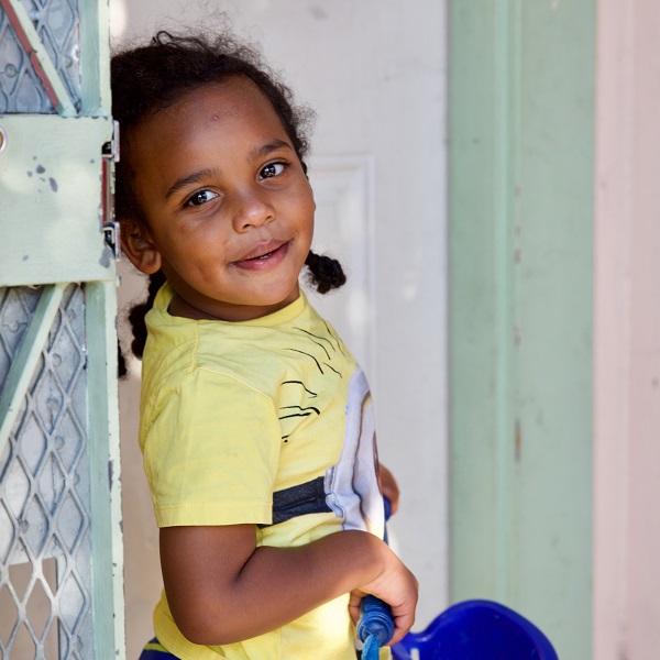 Little girl holding a bucket smiles in a doorway