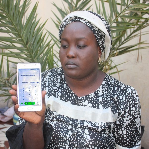 An African woman shows her phone with her Matontine savings numbers displayed