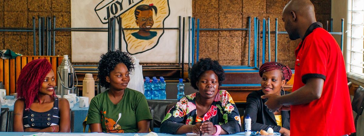 A group of four African women gather at a table with a light blue tablecloth