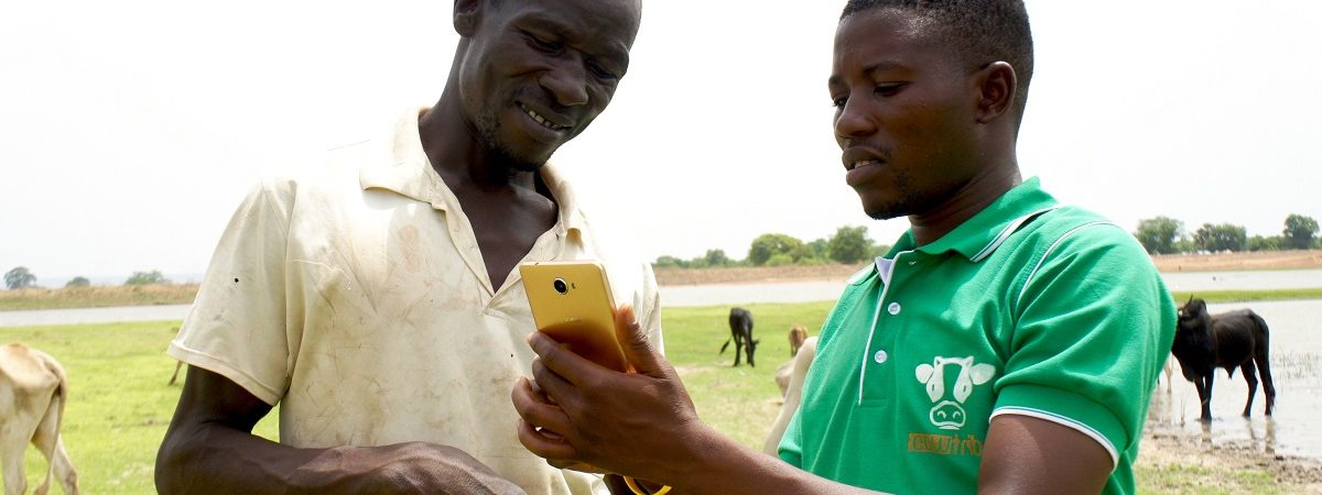 A member of CowTribe demonstrates how to use the mobile platform on his cell phone to a farmer in Ghana