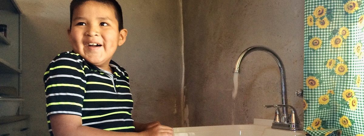 A Native America boy smiles as he washes his hands in his sink with clean flowing water