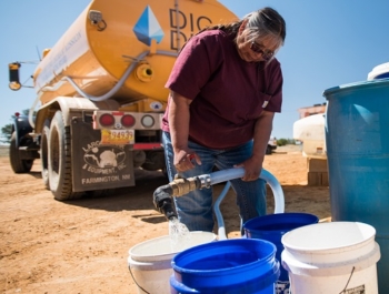 A native american woman fills buckets with clean water. The water is coming from a yellow DIGDEEP water truck.