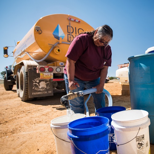 A native american woman fills buckets with clean water. The water is coming from a yellow DIGDEEP water truck.