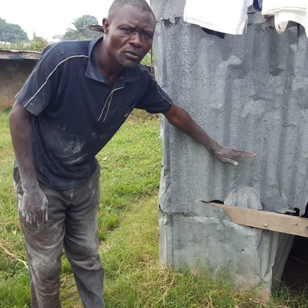 A man shows the destruction of his home and hold his hand to the side of the building to indicate how high the flood waters rose