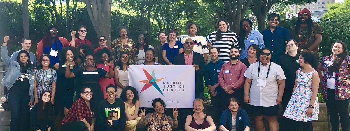 A large group of Detroit Justice Center affiliates gather outside with a DJC banner