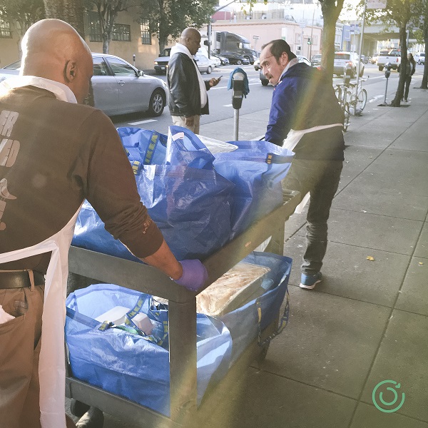 3 men work together to push a cart of replated meals