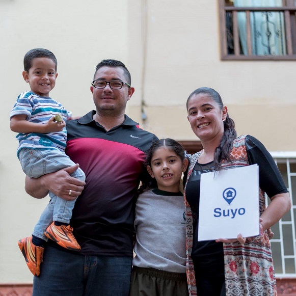 A smiling family of four stands in front of their home in Latin America