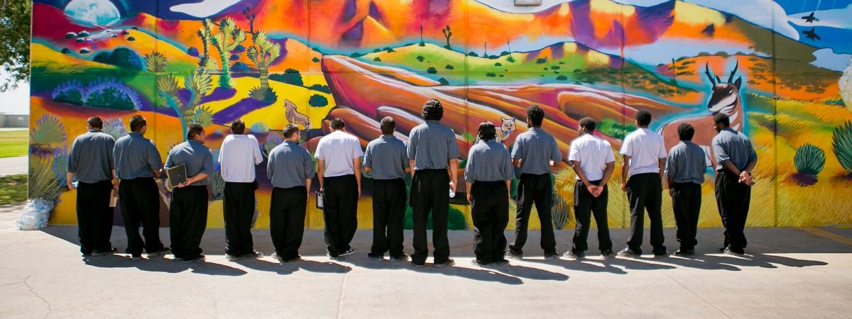 A group of AIYN youth stand facing a colorful mural on a wall