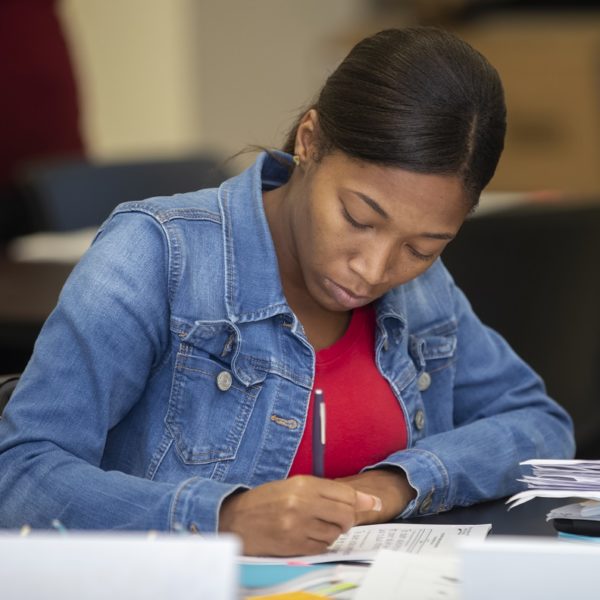 A young black female teacher works at a desk in a school