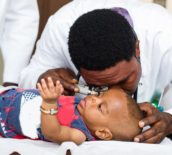 Doctor in a white coat looks in the baby's ear with a device in his office.