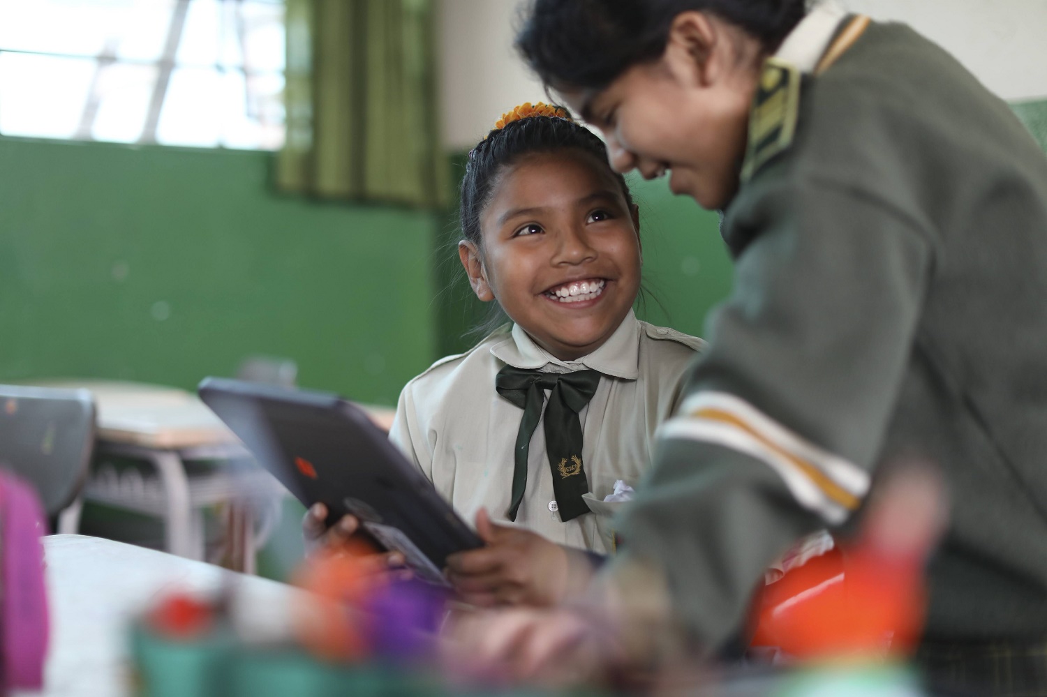 Two children smile while looking at their learning device
