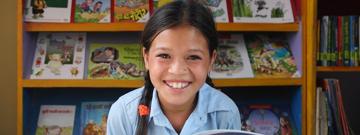 Cambodian student smiles while reading a book in her classroom library
