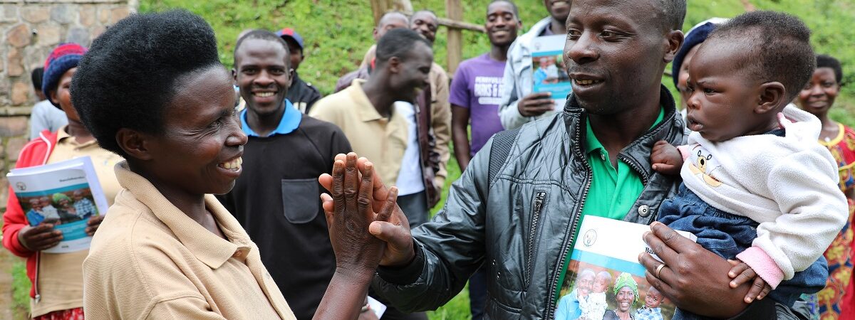 A Rwandan woman and man smile and high five while the community smiles in the background