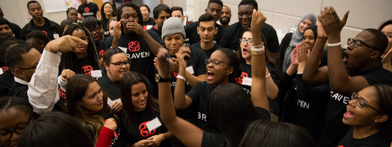 Group of Braven fellows gathered in a group cheering. Each is wearing a black shirt that reads 