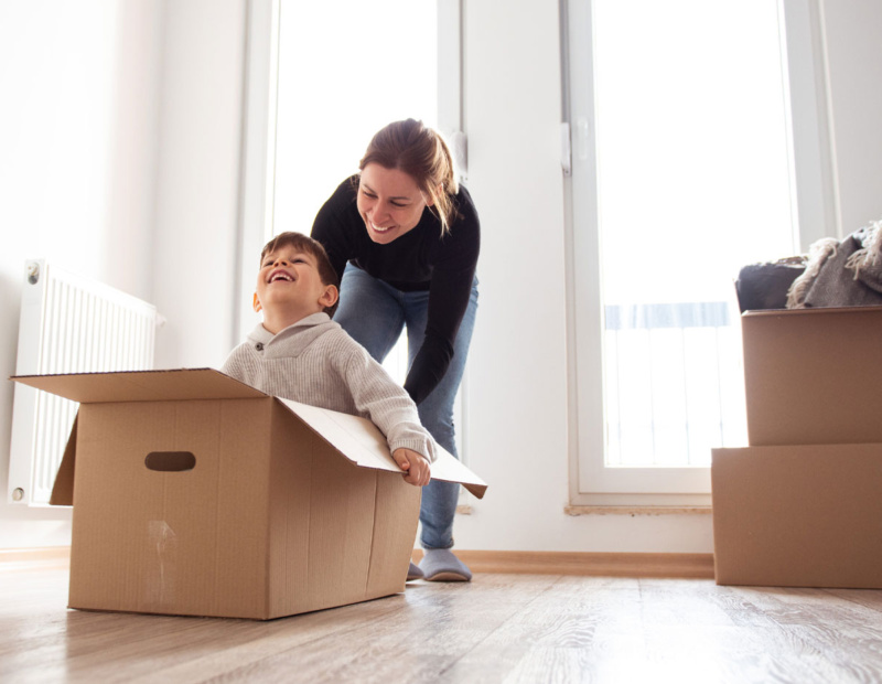 Smiling woman pushing a young boy who is sitting in a moving box.