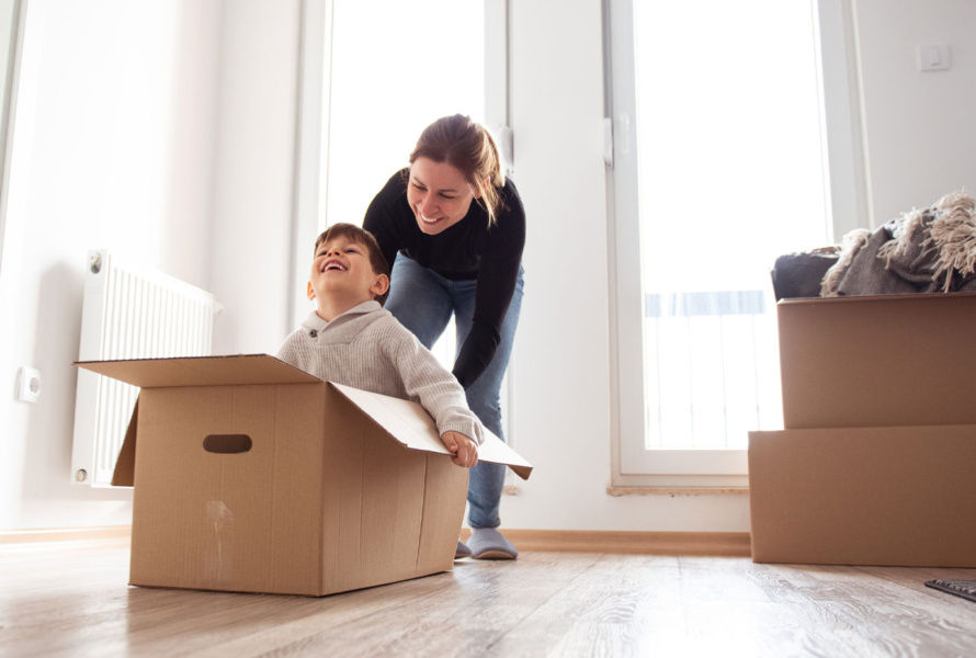 Smiling woman pushing a young boy who is sitting in a moving box.