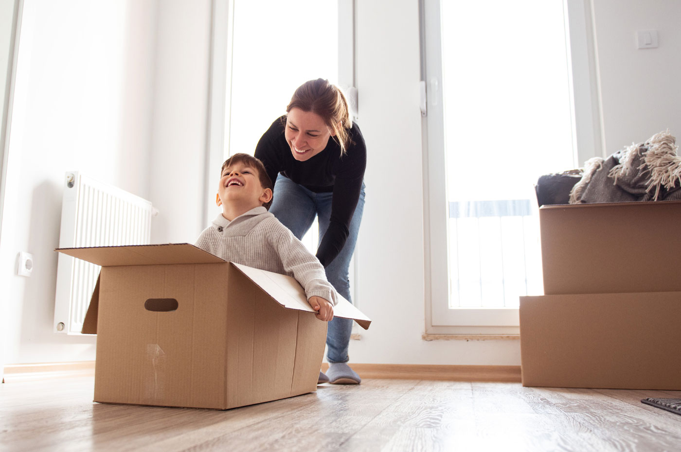 Smiling woman pushing a young boy who is sitting in a moving box.