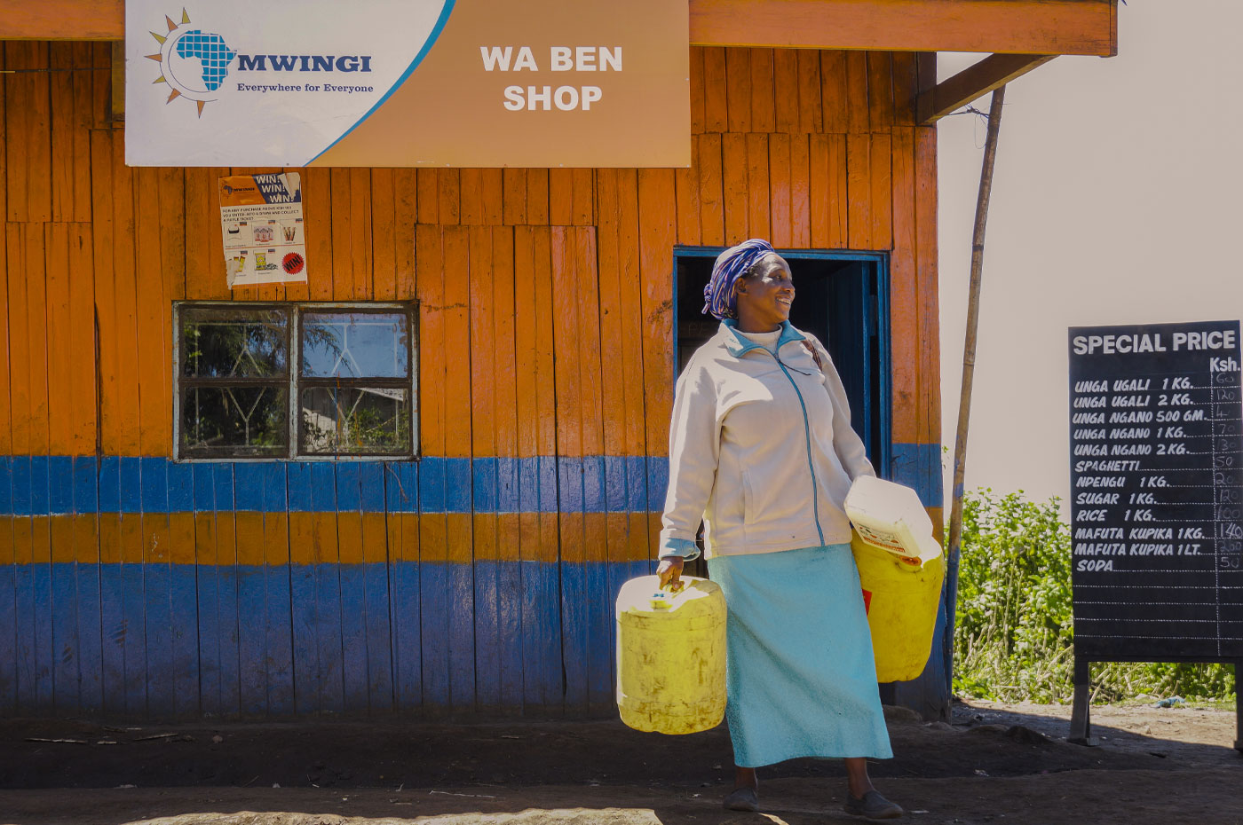 Smiling African woman holding large containers outside of a MWINGI shop.