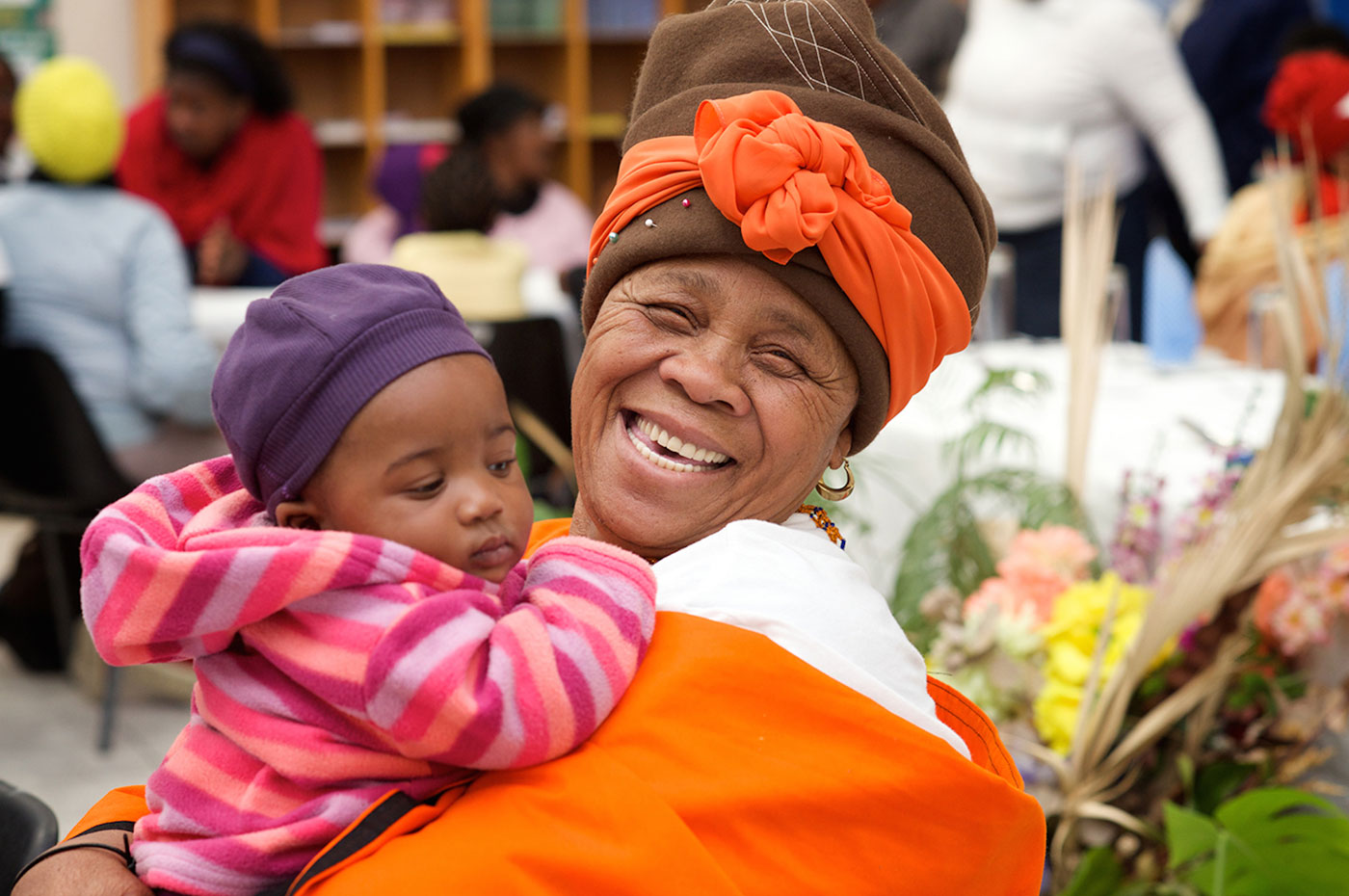 Smiling African woman with bright orange clothing holding a young child.