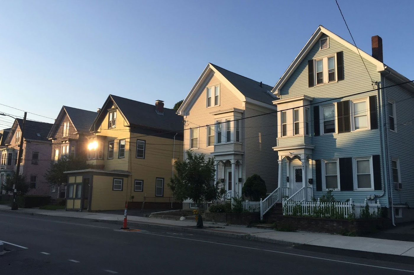 Five multi-story, colorful neighborhood homes in a row with sunlight reflecting off of a window.