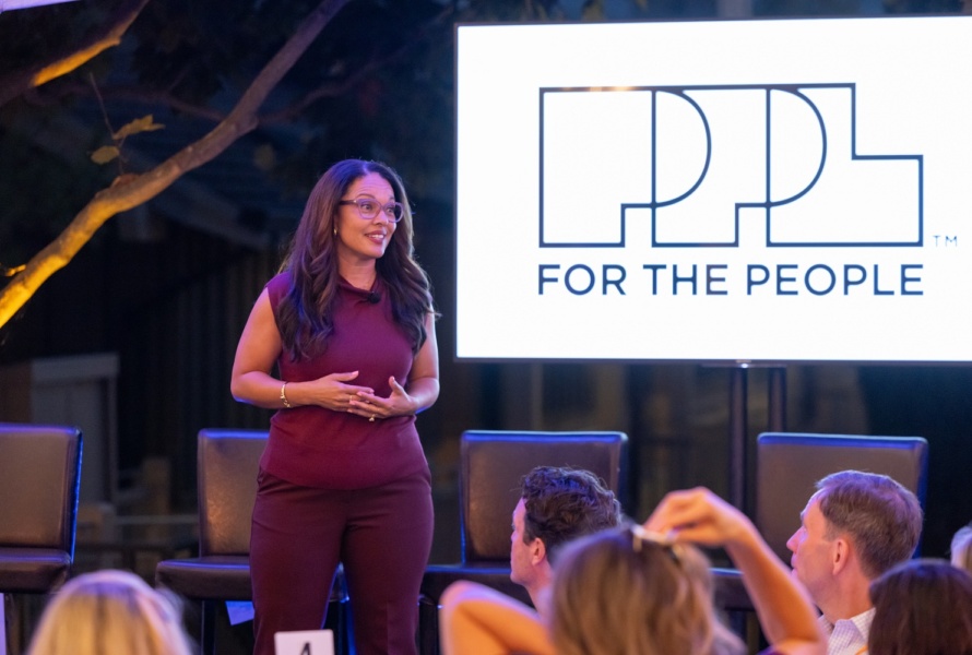Hilary Blout, founder of For The People, stands on stage and speaks to an engaged audience