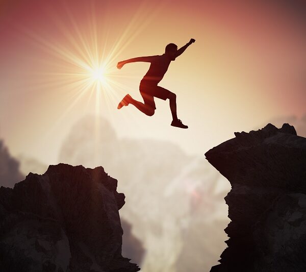 Silhouette of young man jumping over mountains and cliffs at sunset.