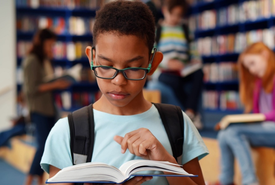 Smart african-american student boy reading book in library, portrait of afro schoolboy preparing for test or exam in school library. Education and knowledge concept