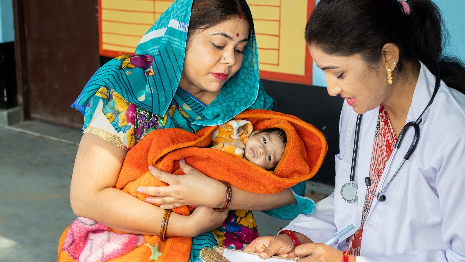 Indian pediatrician doctor examine new born baby at village, Mother wearing sari get infant check by medical person. Rural healthcare camp concept.
