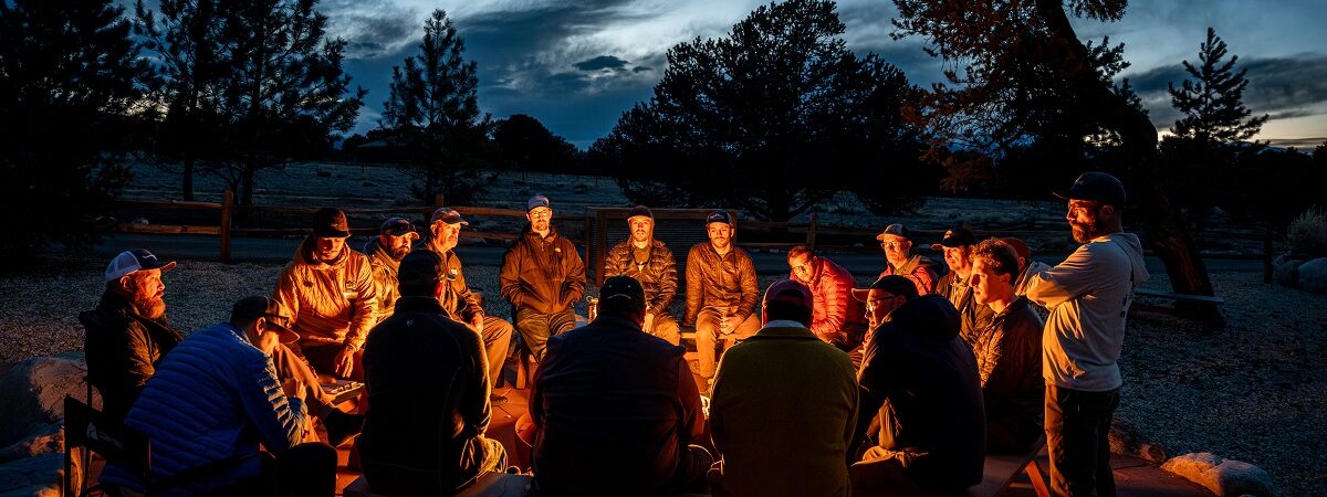 A group of twelve men sit around a campfire at night and talk about their feelings