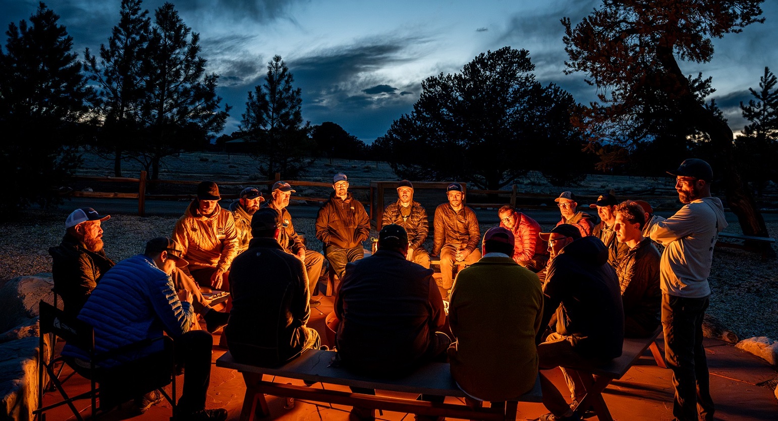 Men around a campfire at night discussing their feelings