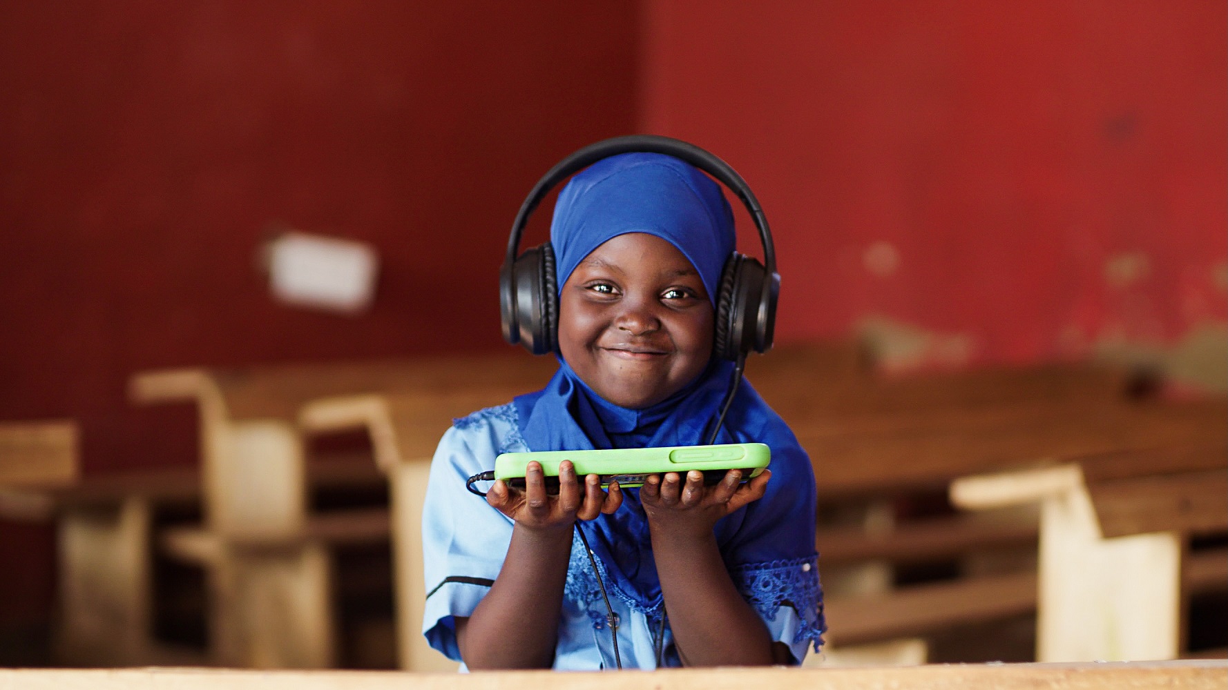 A young, female student in Africa smiles holding up her learning device