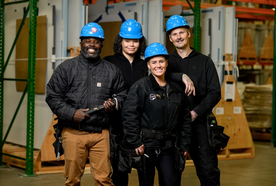 Workers stand smiling on the job. All wear blue hard hats.