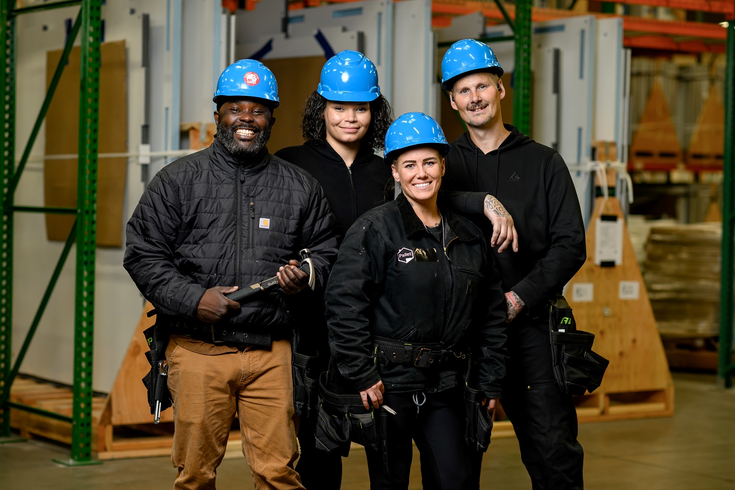 Workers stand smiling on the job. All wear blue hard hats.