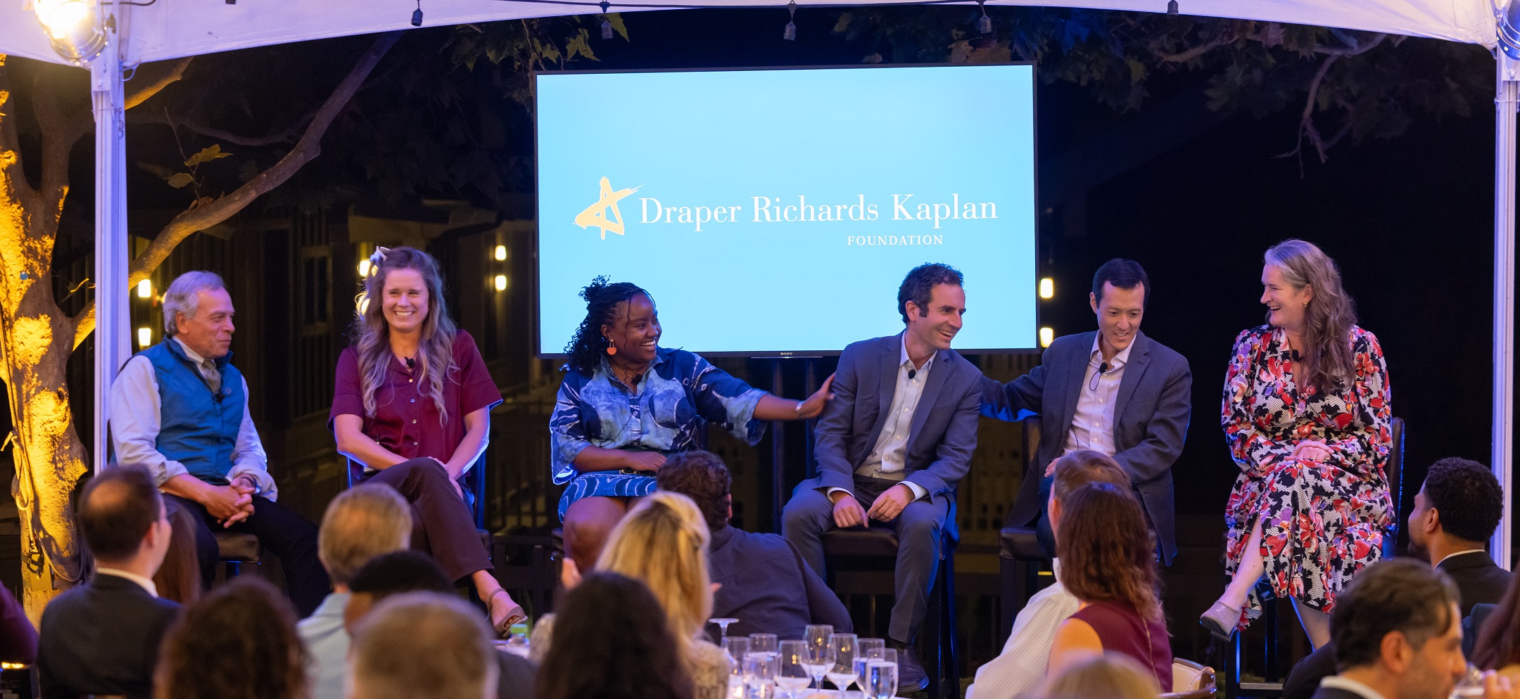 A panel of six people sit on stage at a DRK event